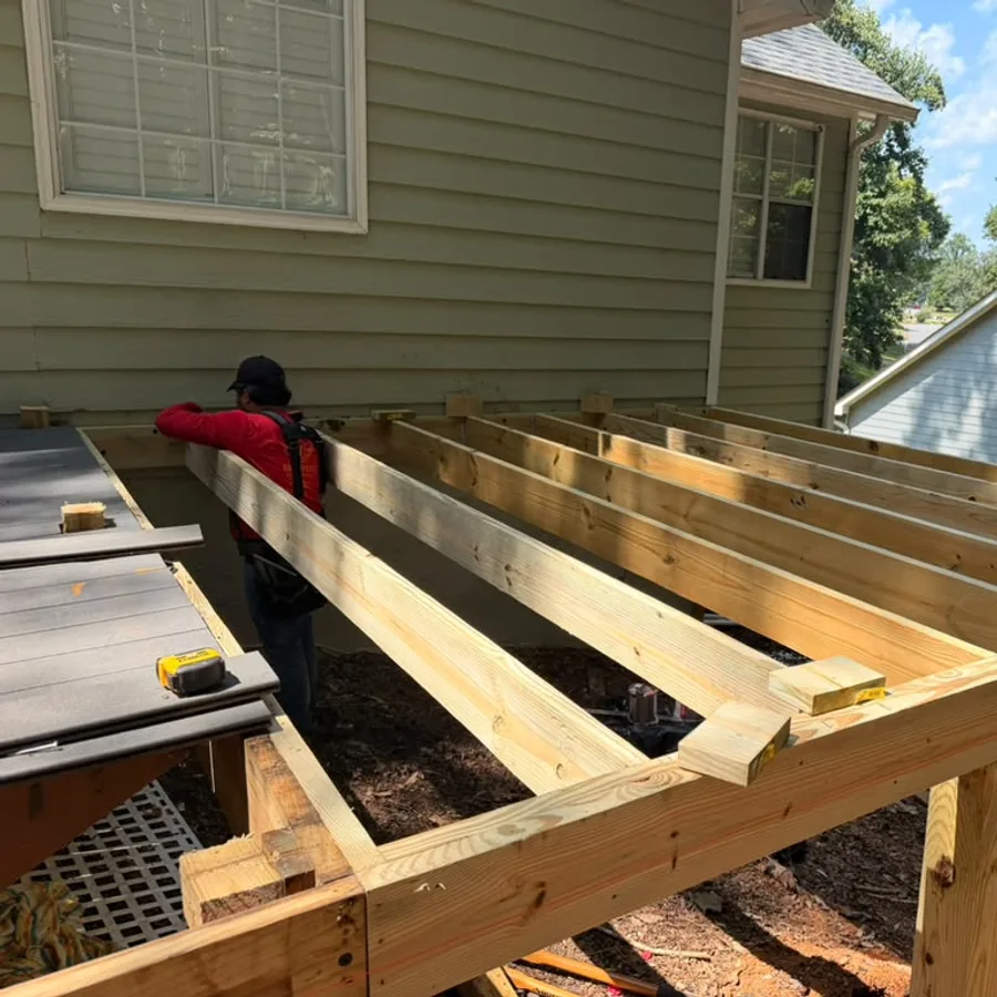 Brothers Remodeling crew member measuring new deck framing along the back of a home