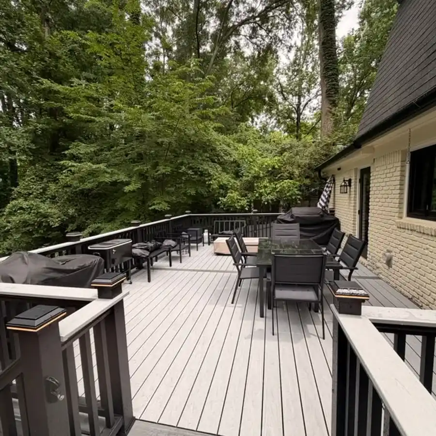 Gray composite deck with black railings and dining set behind a brick home, surrounded by trees