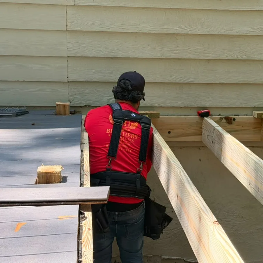 Brothers Remodeling crew member rebuilding deck framing with new pressure-treated joists next to composite decking