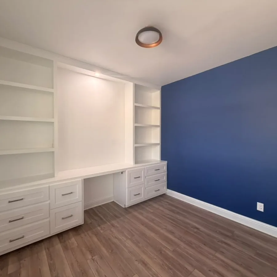 Home office with a deep blue accent wall and white built-in cabinets