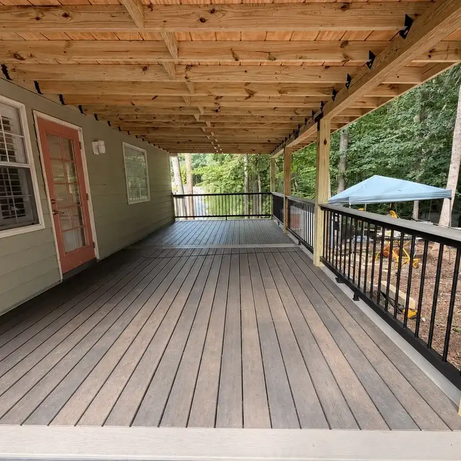 Covered porch with composite decking, exposed wood framing overhead and black railings